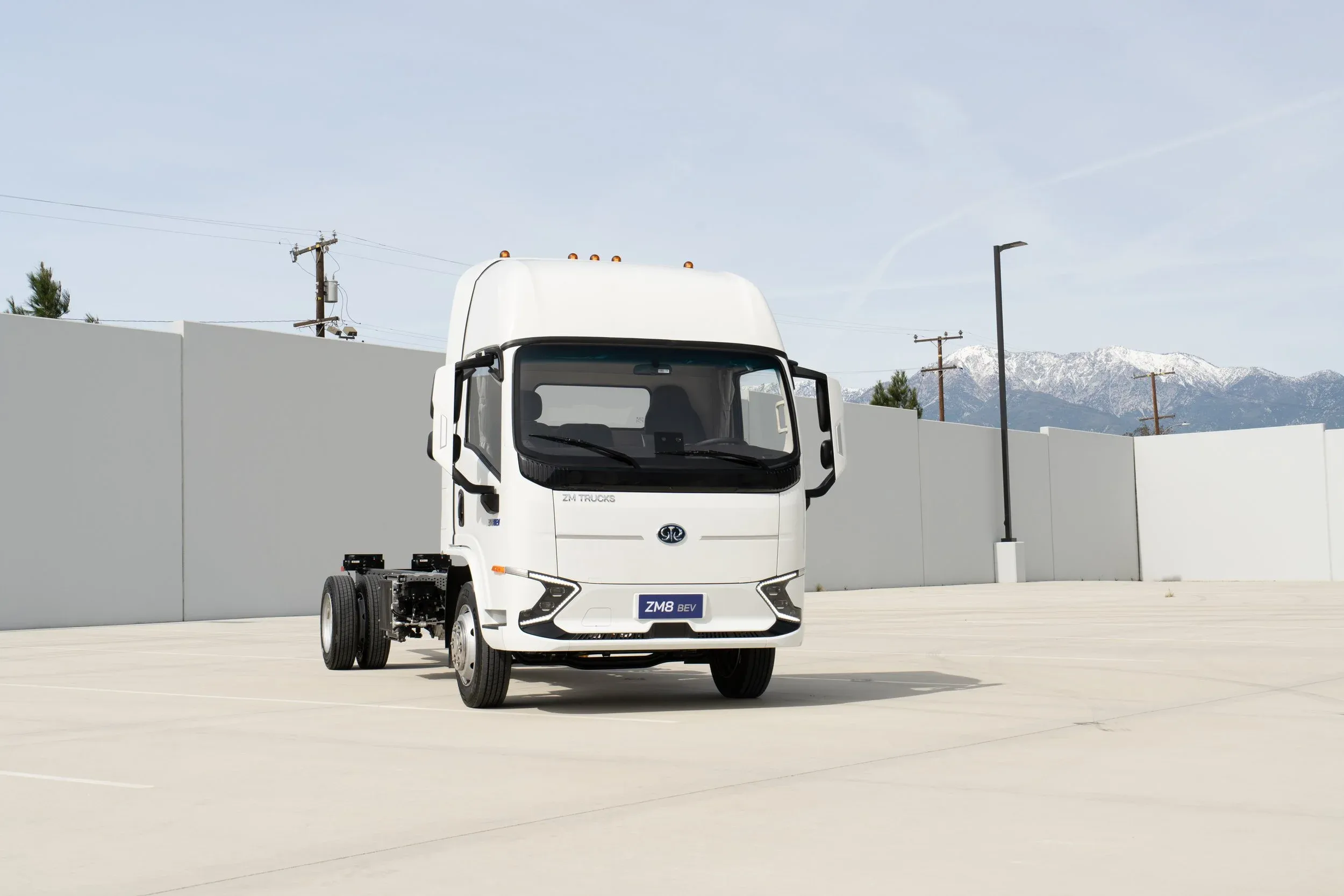 Electric truck with a white cab on a concrete lot with mountains behind it